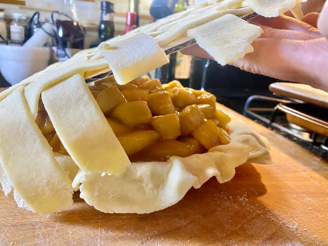 A lattice pie crust being applied to an apple pie.