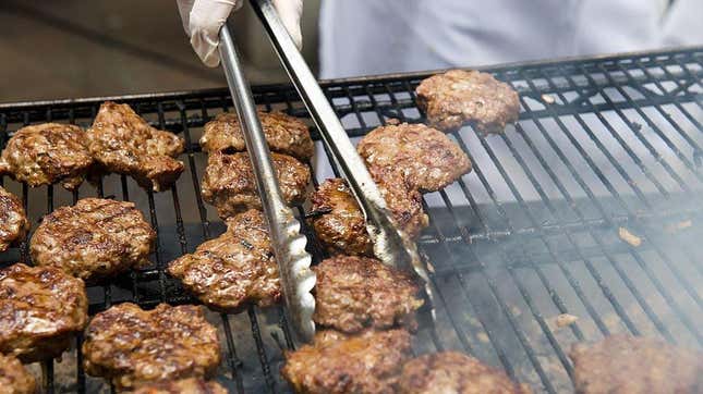 Person with tongs flipping burgers on grill