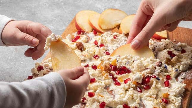 Adult and child's hands dipping apples into sweet butter board