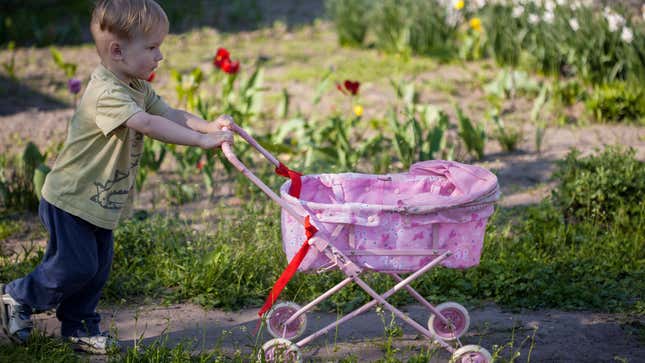 Toddler boy pushing a toy stroller through a park