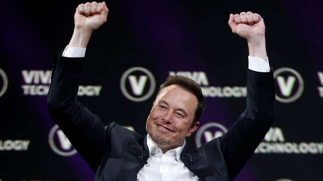 Elon Musk in a suit with no tie holding his hands up over his head. Background is the logo for the Viva Technology Conference.
