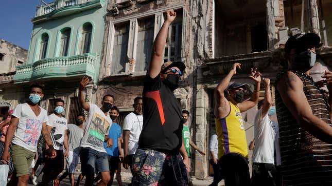 Cuban protesters walk with their fists raised past the colorful and crumbling facades of buildings in Havana.