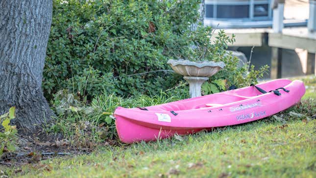 A disused kayak sitting in the grass next to a bird feeder