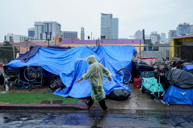 Homeless people use plastic tarps to shield themselves from a light rain brought by Tropical Storm Hilary in downtown San Diego, on Sunday, August. 20, 2023.