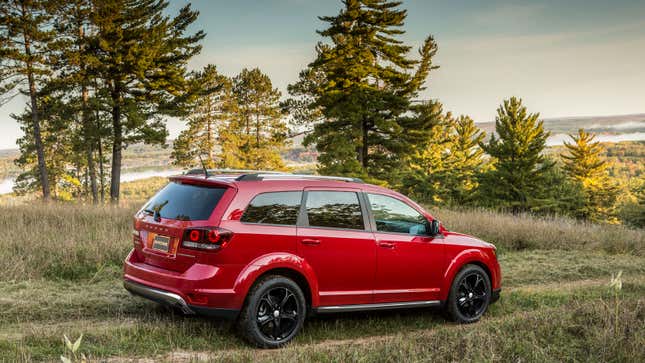 A photo of a red Dodge Journey SUV driving in a field. 