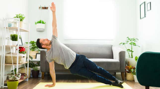 A man in his living room performs a lateral stretch while using a yoga mat