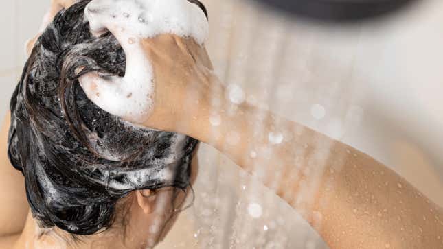 woman lathering up hair with shampoo in shower