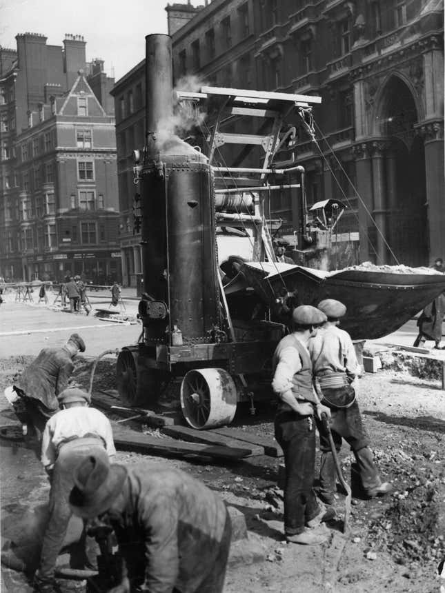 Circa 1925: Workmen repairing a road, with the aid of a cement mixer.