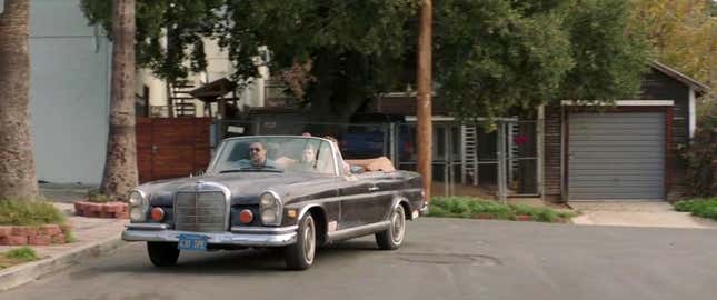 A brown Mercedes-Benz 280se convertible is being driven by Ryan Gosling. Russel Crowe is in the passenger seat.