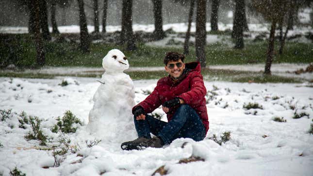 A man poses for a picture next to a snowman outside a forested area in the Sidi al-Hamri region of Libya’s eastern Jebel Akhdar (Green Mountain) upland region, about 200 kilometres east of Benghazi, on February 16, 2021.