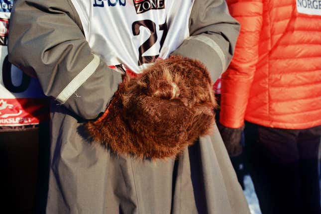 A musher’s assistant keeps warm, waiting for his work to begin.