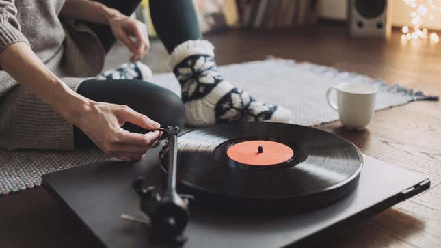 A woman places the needle of a record player onto a record while sitting on the floor relaxing and listening to music