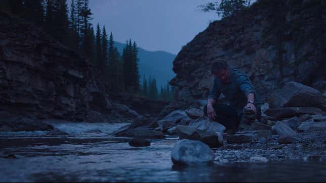 Joel stacks rocks into a cairn near a river in HBO's The Last of Us.