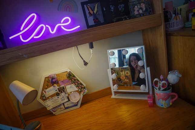 Sara Hunt, 19, a sophomore at New York University from Pigeon Forge, Tennessee, is shown reflected in a mirror on her desk in her dorm room, Wednesday, Aug. 30, 2023, in New York. Hunt wanted her room to look cozy but her budget was $100. She decorated with plants, mementos, and pillows covered with images of her pets. (AP Photo/Bebeto Matthews)