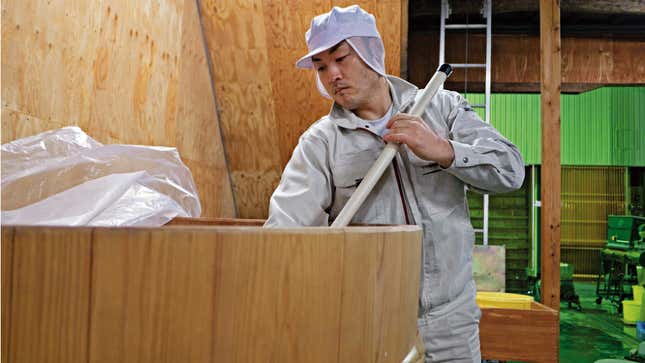 A sake brewer attends to wood brewing tub.