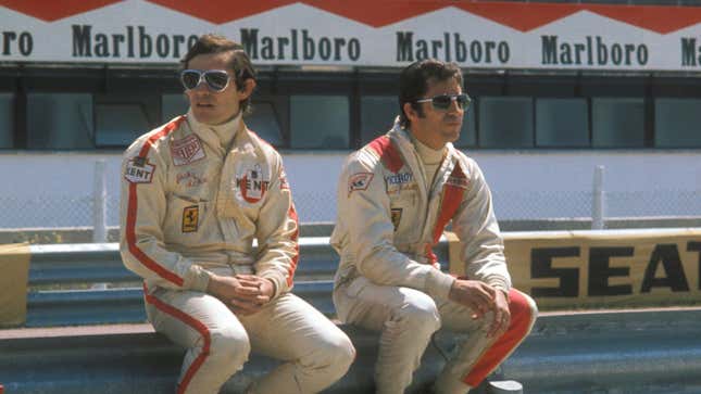 Jacky Ickx and Mario Andretti sit side by side on pit wall