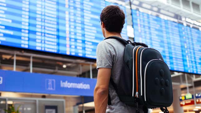 Man wearing backpack looking at flight status screen at airport