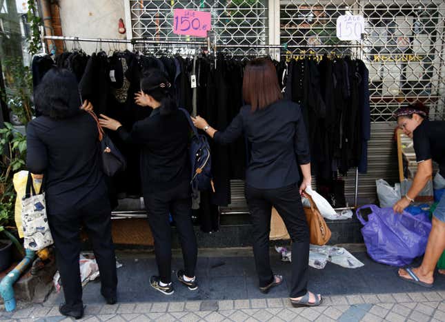 Pedestrians dressed in black clothes to mourn the passing of Thailand's King Bhumibol Adulyadejin looks through clothing on a rack along a street in Bangkok, Thailand October 17, 2016. REUTERS/Issei Kato - RTX2P3A9