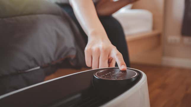 Woman pressing a button on an air purifier in bedroom 