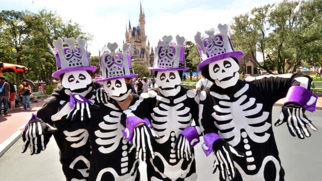 People in skeleton costumes and purple hats stand in front to Cinderella's Castle at Tokyo Disneyland.
