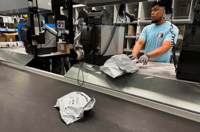 A man working next to a conveyer belt, onto which he is pushing Amazon packages.