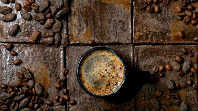 cup of coffee on brown tile table with coffee beans