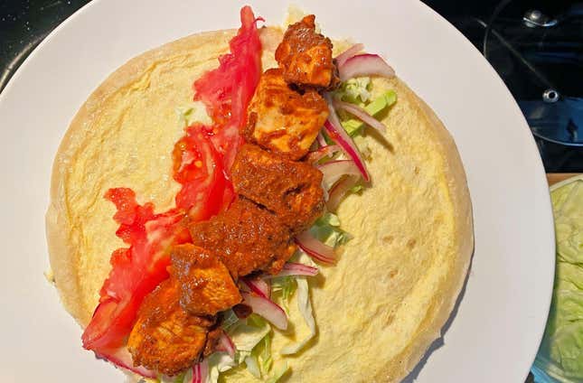 Layered chicken frankie with masala chicken chunks, sliced tomato, cabbage, and pickled onion.