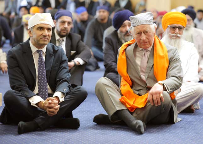 FILE - Britain&#39;s King Charles III, right, sits on the floor next to Professor Gurch Randhawa, a member of the Sikh Congregation, in the Prayer Hall during the king&#39;s visit to the newly built Guru Nanak Gurdwara, in Luton, England, Tuesday, Dec. 6, 2022. A year after the death of Queen Elizabeth II triggered questions about the future of the British monarchy, King Charles III’s reign has been marked more by continuity than transformation, by changes in style rather than substance. (Chris Jackson/Pool Photo via AP, File)