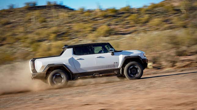 A photo of a white Hummer EV driving on dirt. 