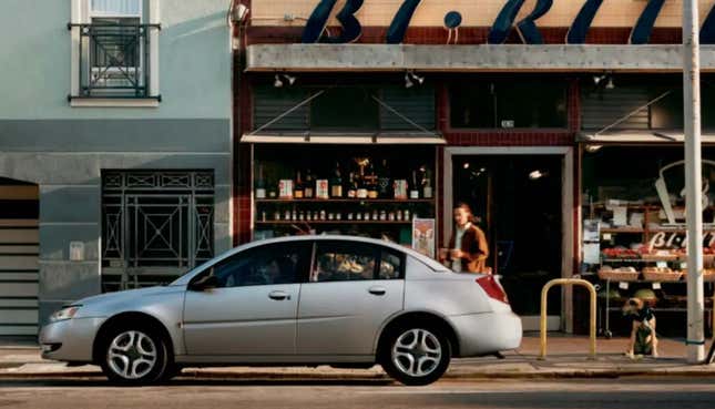 A silver Saturn Ion sits parked in front of a bakery on a city street.