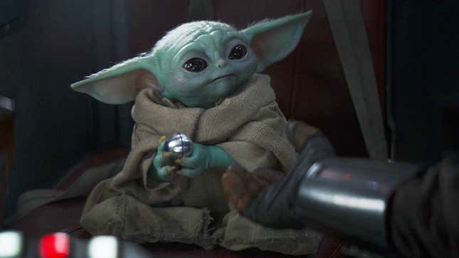Baby Yoda aka Grogu holds onto a silver ball while sitting in a spaceship. 