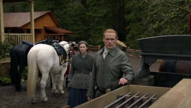 Claire and Jamie Fraser stand beside some horses in a scene from Outlander.