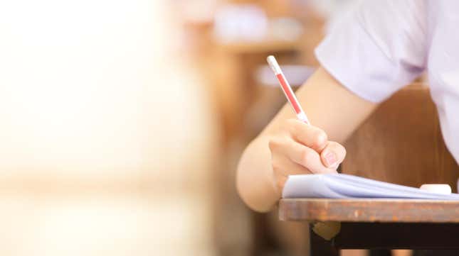 Student at desk, holding pencil, writing on paper 