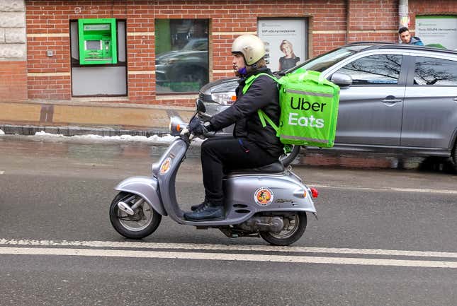 A delivery driver rides a motorized scooter with a large, green, Uber-branded backpack on.