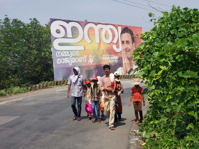 A Christian family walks past a billboard depicting Rahul Gandhi during the Good Friday Via Crucis procession.
