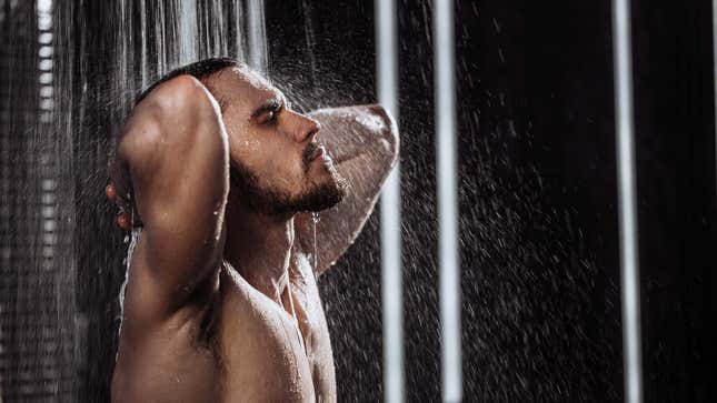 A young man washes himself in a large shower. 