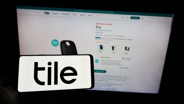 Person holding mobile phone with logo of US consumer electronics company Tile Inc on screen in front of business web page Focus on phone display