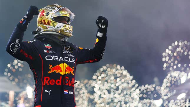 A photo of Max Verstappen with his arms in the air and fireworks behind him. 
