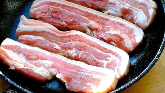 Raw bacon cooking in a cast-iron pan