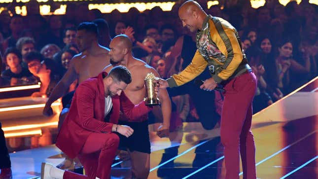 Zachary Levi presumably offering a tub of golden popcorn to the Rock in exchange for a cameo in his movie at the MTV Movie Awards