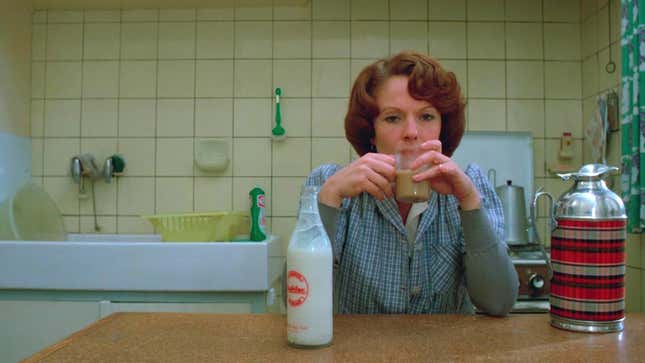 A screenshot from Jeanne Dielman, 23 quai du Commerce, 1080 Bruxelles of the title character sitting in her kitchen drinking milk