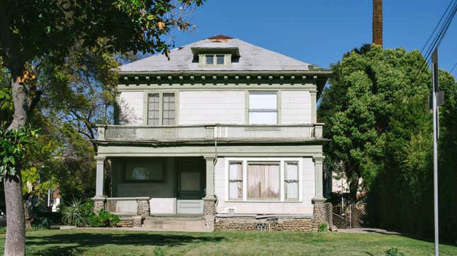 A stately but aging home in need of obvious roof, siding, and window repair.