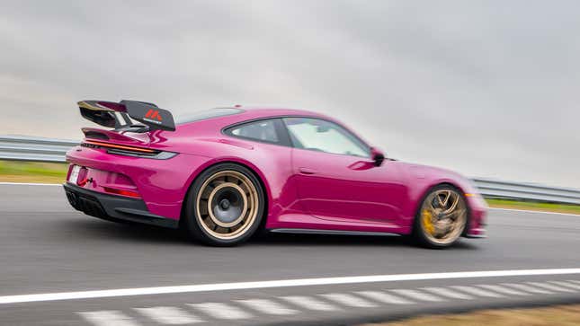 A ruby Porsche 911 GT3 equipped with the Manthey Performance Kit driving on a track, viewed from the rear quarter.