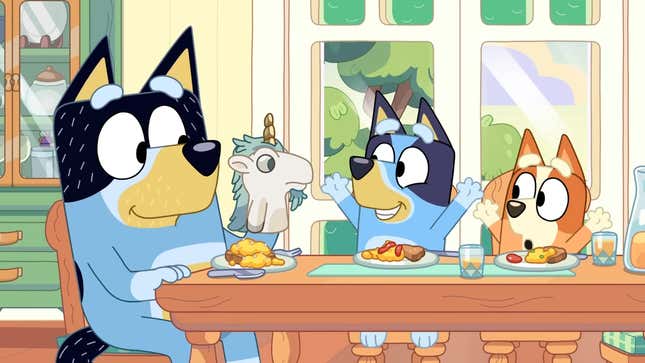 A screenshot from the Bluey season 3 trailer with Bluey, Bingo, and Bandit sitting at the dining table. Bandit is wearing a unicorn puppet on one paw