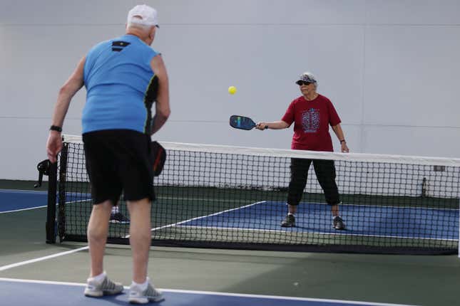 Two seniors play pickleball on a court. 