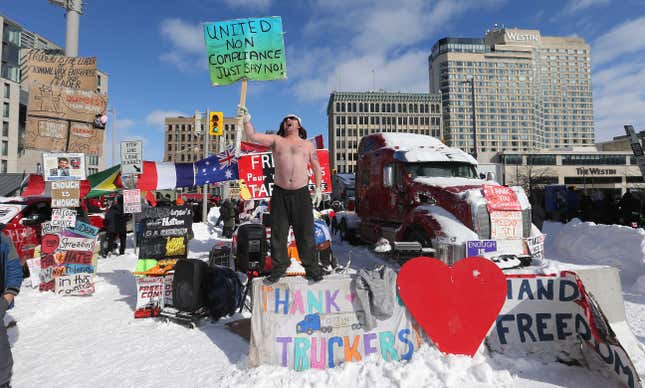 A shirtless man shouts to a blue winter sky on a city street while holding a blue-green sign that reads "United non compliance just say no"