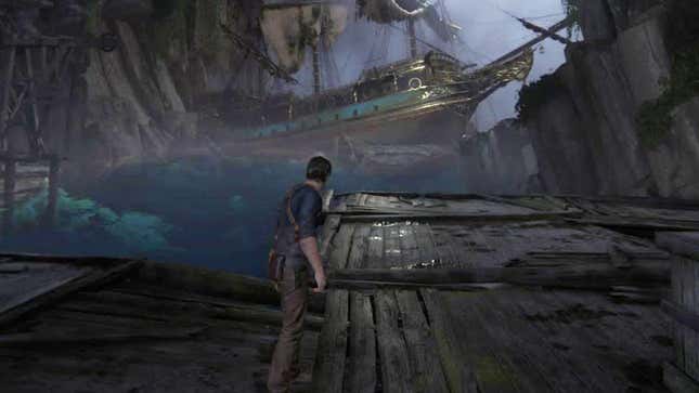 Nathan Drake stands in a dark, water-filled cave before a very large pirate ship in Uncharted 4.