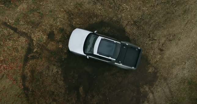 A Rivian RT1 electric truck turns in a narrow circle, known as a tank rotation.  The image was taken from above and shows deep marks on the ground made by the stuntman. 