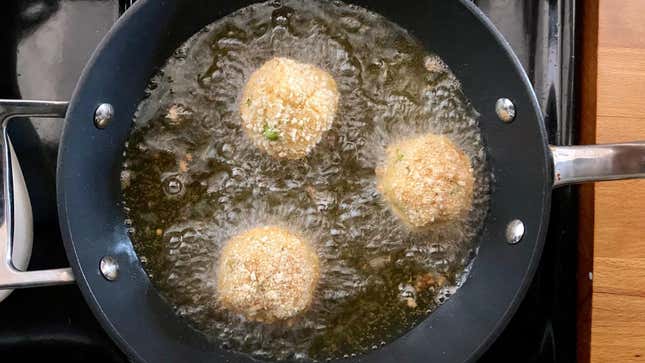 Arancini frying on their first side.