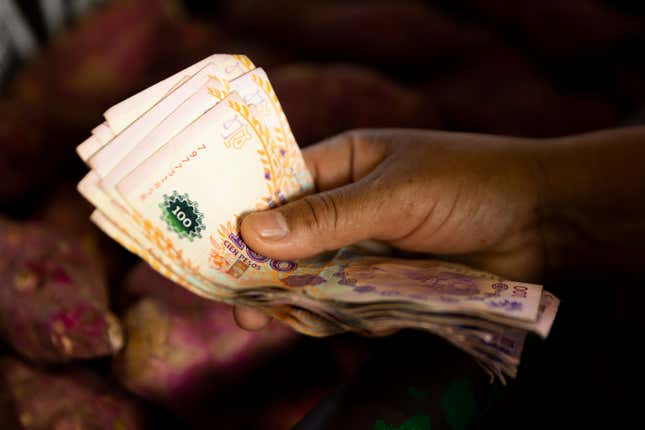 A closeup of a hand holding 100 Argentine pesos bills.